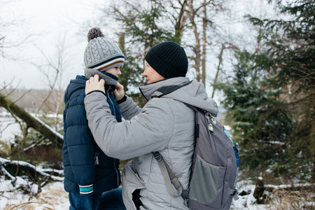 Father adjusting sons scarf during winter forest hikeの写真素材