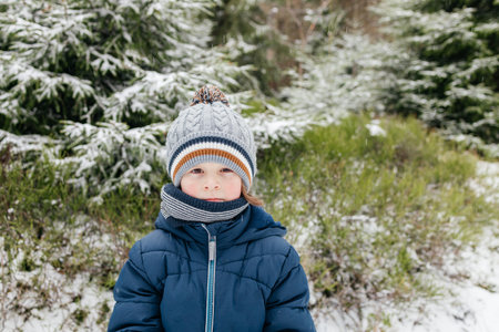 Young boy wearing winter clothes standing in snowy forest