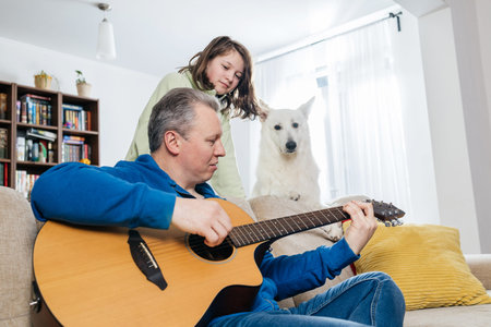 Father playing acoustic guitar with daughter and dog at home
