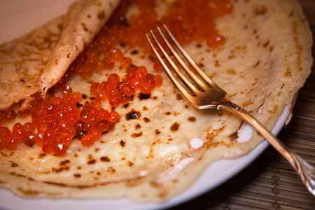 Traditional Russian pancake with red caviar. Fork, wooden table. Maslenitsa. Selective focus.の写真素材