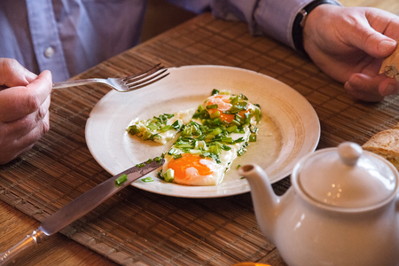 Man eating his breakfast eggs with biscuits. Wooden table. Knife and fork.の写真素材