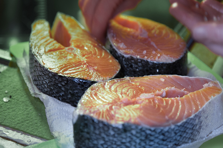 Raw salmon fillet. Three fresh salmon steaks.Cooking salt.Cutting board. Woman hands.の写真素材