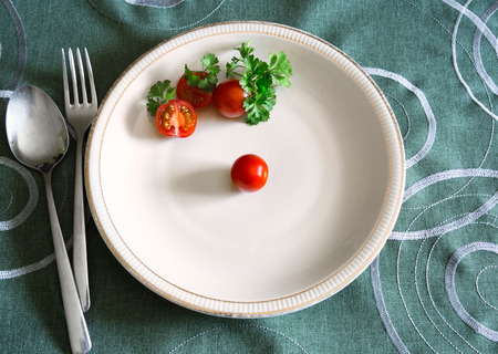 Three cherry tomatoes and parsley leaves on white plate. Food conceptの写真素材