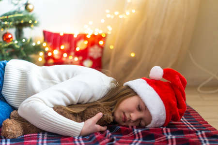 Cute little girl sleeping on floor under the Christmas Tree waiting for Santa Claus to come. Selective focus.の写真素材
