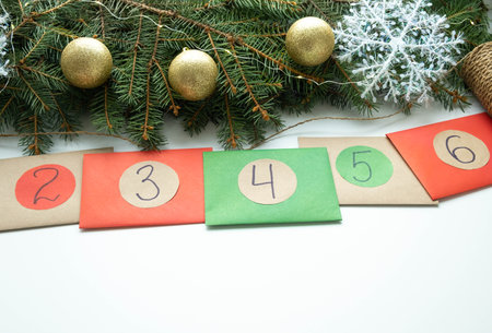 Homemade Christmas Advent Calendar, multicolored envelopes with numbers lie on white background near green spruce branches and balls. Copy space for text.の写真素材