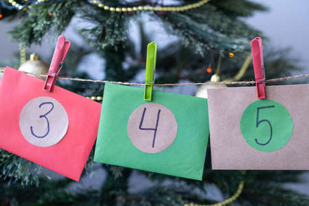 Close up Christmas Advent calendar with colorful envelopes three, four, five near Christmas tree. Homemade surprise for children.の写真素材