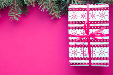 Merry Christmas and Happy New Year gift on hot pink background with green fir branches. Christmas tree and present flatly. Flat lay, top view, copy space for text.の写真素材