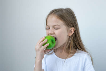 Cute little girl in white T-shirt eating green apple. Health care, fruits, healthy eating, dental...