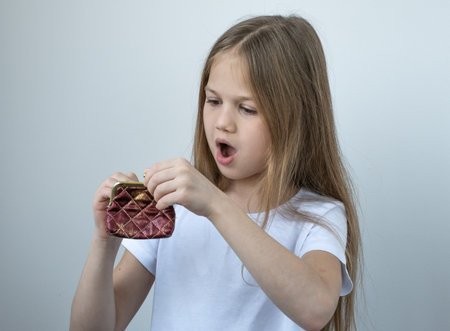 Little girl opens the wallet, sees that it is empty and surprised. Learning financial responsibility...