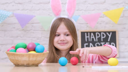 Funny little girl with bunny ears play Easter hare hunter at home. Kid rabbit hunts for eggs. Happy family Easterの写真素材