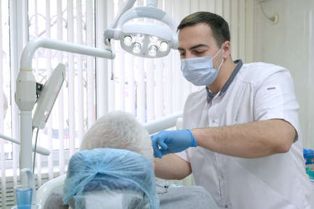 Professional dentist in protective mask working with elderly patient in clinic. Senior man getting treatment at dental office. Doctor working with client's teeth. health care and medicine conceptの写真素材