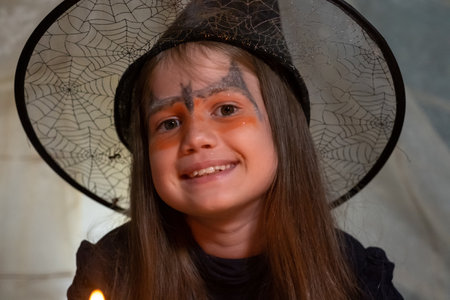 Cute little girl in witch costume on Halloween smiles looking at camera at night. Portrait of kid in...