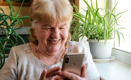 Happy smiling elderly woman using her phone at home. Grandma is typing text message on her...