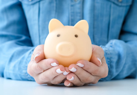 Woman in a blue shirt holding piggy bank on white table. Saving money conceptの写真素材