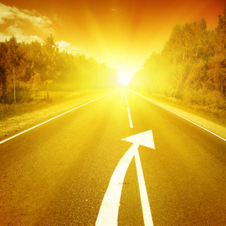 Country road with arrow sign on asphalt and sunset の写真素材