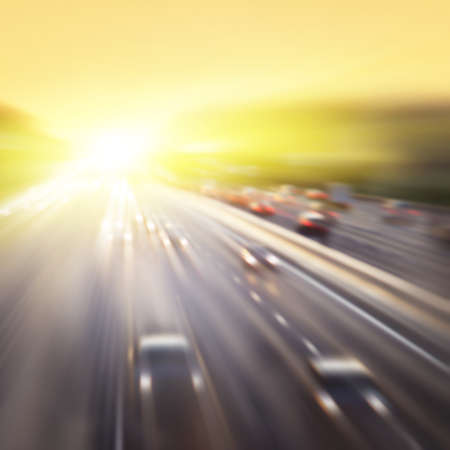 Cars in motion blur on highway during sunset.