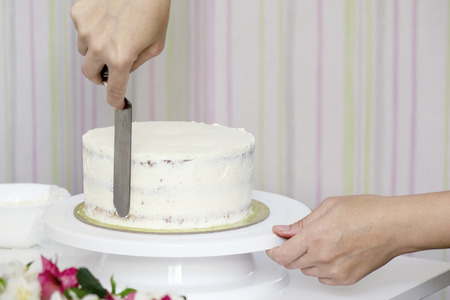 The confectioner's hands decorate the cake with a white tasty creamの写真素材