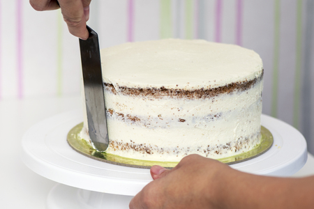 The confectioner's hands decorate the cake with a white tasty creamの写真素材