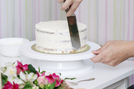 The confectioner's hands decorate the cake with a white tasty creamの写真素材