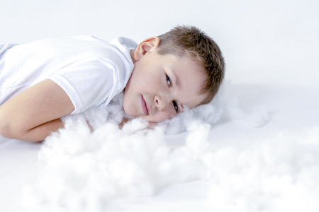 boy in white t-shirt is lying on his stomach on white artificial snow on a white backgroundの写真素材