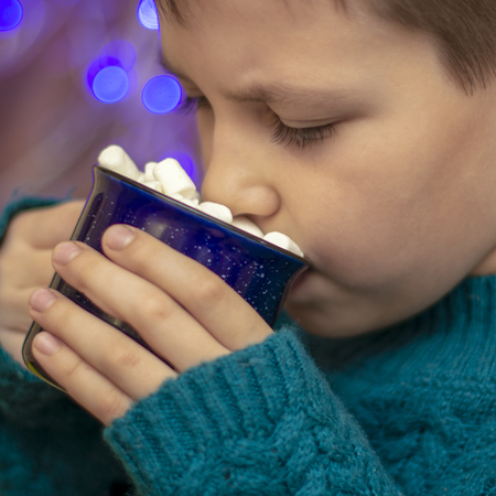 boy drinking cocoa with marshmallows cozy bokeh backgroundの写真素材