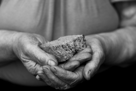 an old grandmother holds a crust of bread in black and white photography with two wrinkled hands.の写真素材