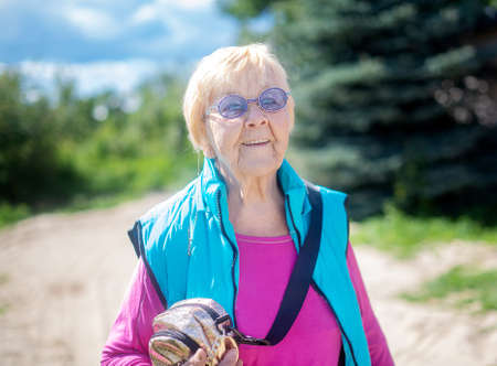 Happy, fashionable 90-year-old grandmother with gray hair, sunglasses and a smile in nature on a...