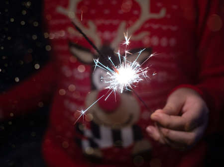 Christmas party. A child holds a lit firework on a shiny background with bright gold Christmas...