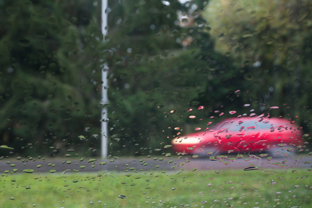 Rain drops on car glass, focus on raindrops. View to the street and car in motion. Long exposure photoの写真素材