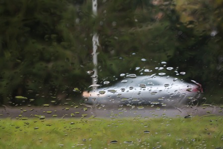 Rain drops on car glass, focus on raindrops. View to the street and car in motion. Long exposure photoの写真素材