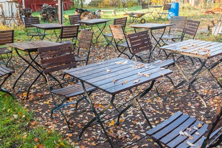 Beautiful autumn in old outdoor cafe in the park - wet tables and chairs with colorful foliage.の写真素材