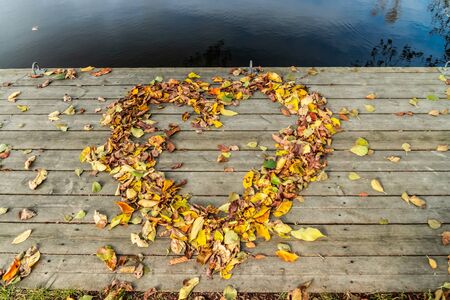 Dried autumn leaves in form of heart on the wooden pier.の写真素材
