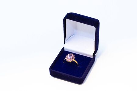 Golden ring with purple gemstone in a blue jewelry box on white background