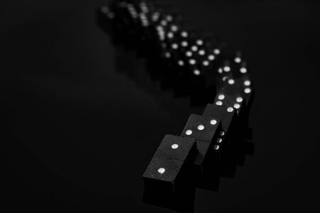 Black vintage falling dominoes on a black background, selective focus. WB photo.の写真素材