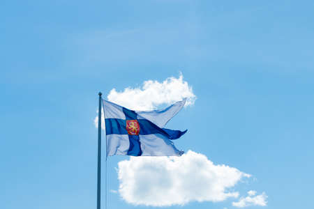 State flag of Finland with national coat of arms against blue sky on the windの写真素材