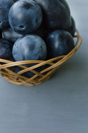 Garden plums in a wicker basket on a gray background. Useful summer fruits.の写真素材