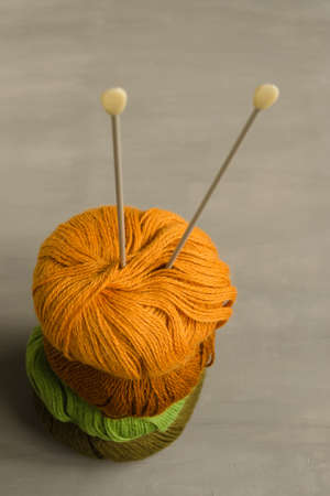 Orange, brown, green and marsh woolen yarn and knitting needles on a gray backgroundの写真素材