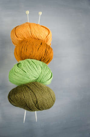 Orange, brown, green and marsh woolen yarn and knitting needles on a gray backgroundの写真素材