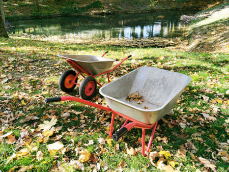 Empty metal gray wheelbarrow in the park. Collection of autumn leaves, garbage collection, sand...