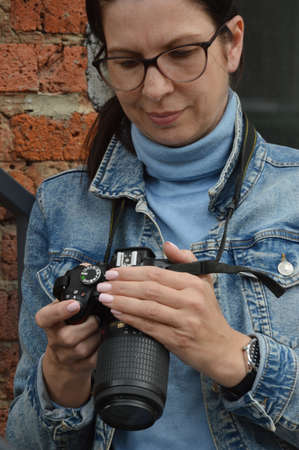 A young woman photographer in a blue denim jacket and glasses stands against the background of a...