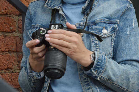 Womens hands are holding a camera. A girl in a denim jacket looks through pictures on a professional camera. Close-up.の写真素材