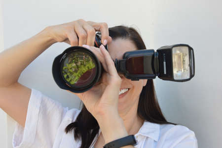 Girl with a camera on a white background. The girl takes pictures and smiles. Hobbies, profession, education.の写真素材