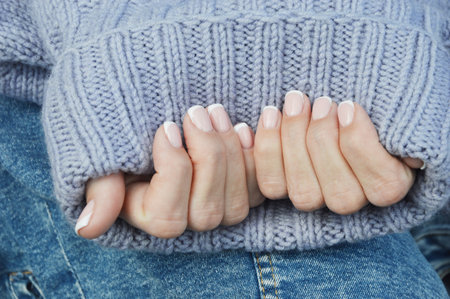 Nails with a beautiful French manicure on the background of a warm knitted sweater. Winter trend,...