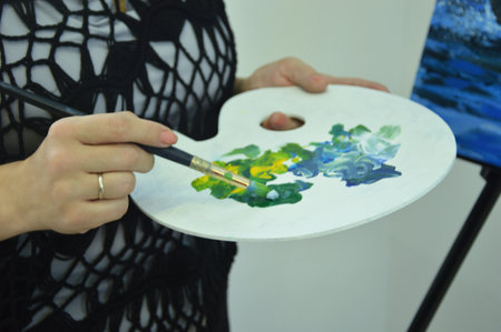 Palette with different colors of mixed paints close-up. The artist takes paint from the palette with a brush for painting.の写真素材