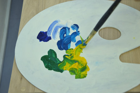 Palette with different colors of mixed paints close-up. The artist takes paint from the palette with a brush for painting.の写真素材