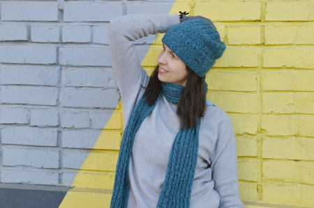 Portrait of a smiling young woman with dark hair in a gray sweater, turquoise hat and scarf stands...