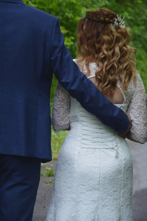 The groom in a blue suit and the bride in a white dress with flowing hair. back view. Newlyweds on a wedding walk.の写真素材