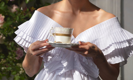 A bride girl in a white dress holds a cup of tea or coffee in her hands. Women's hands with a cup.の写真素材