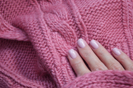 Pink knitted wool scarf, sweater and female hands with professional manicure. Winter hand care.の写真素材