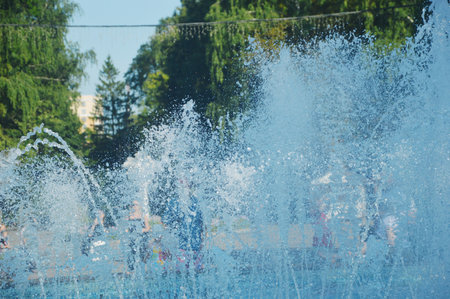 Vertical jets of blue water from a fountain with splashes against a background of green treesの写真素材